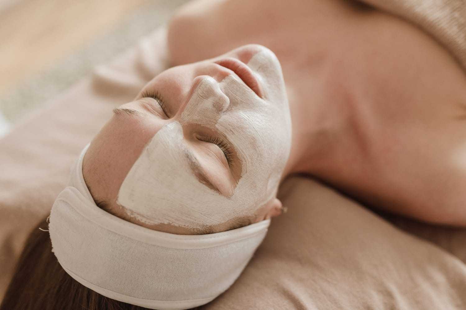 Person relaxing with a face mask applied, lying on a bed with a headband on.