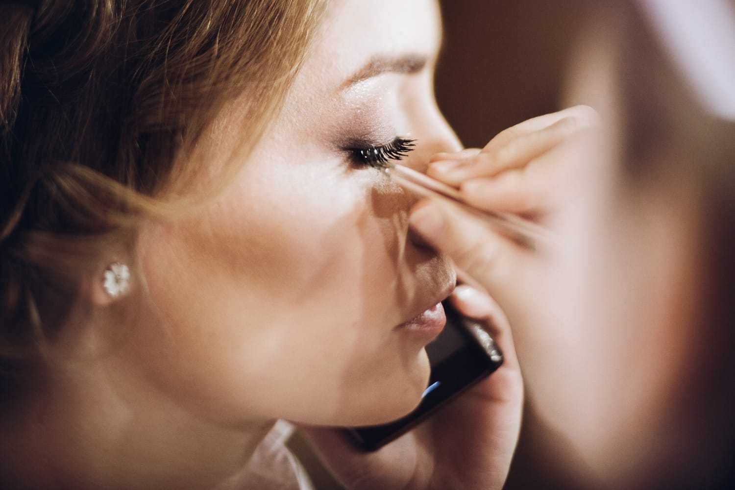 Woman having eyelashes applied with tweezers during beauty treatment.