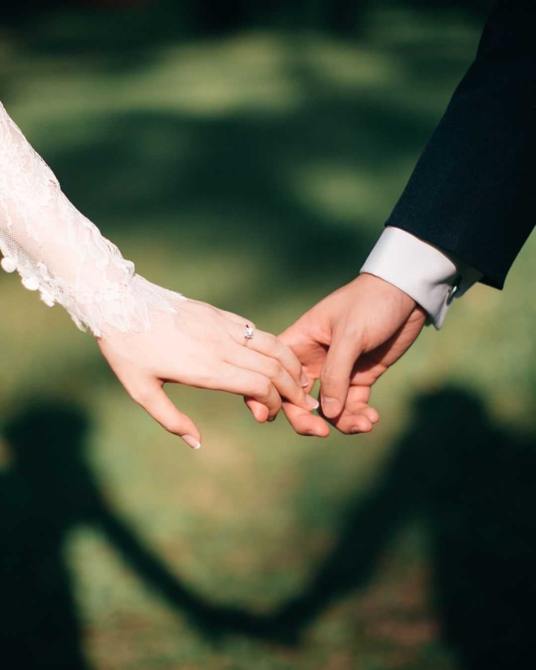 Close-up of a couple holding hands, shadows forming a heart shape on the ground.